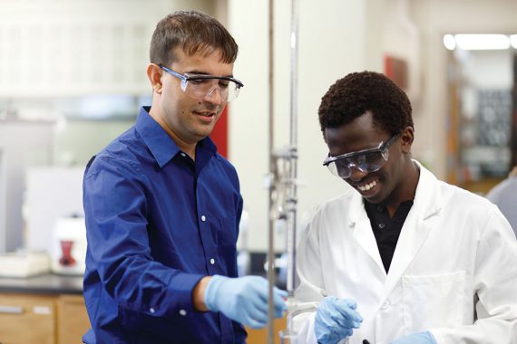 Two men wearing safety glasses work in a lab.