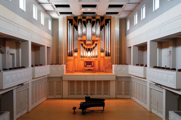 Photograph of a pipe organ built into the wall on a stage in an intimate theater setting.